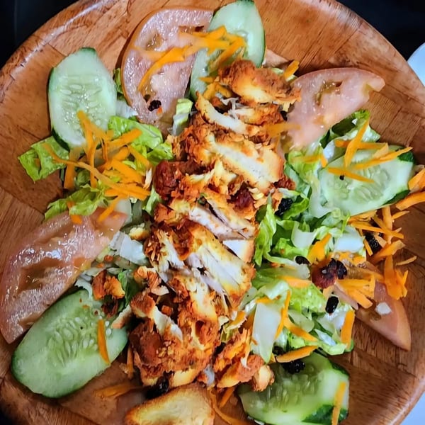 Crispy fried chicken salad with lettuce, cucumber, tomato, and shredded carrots in a wooden bowl.