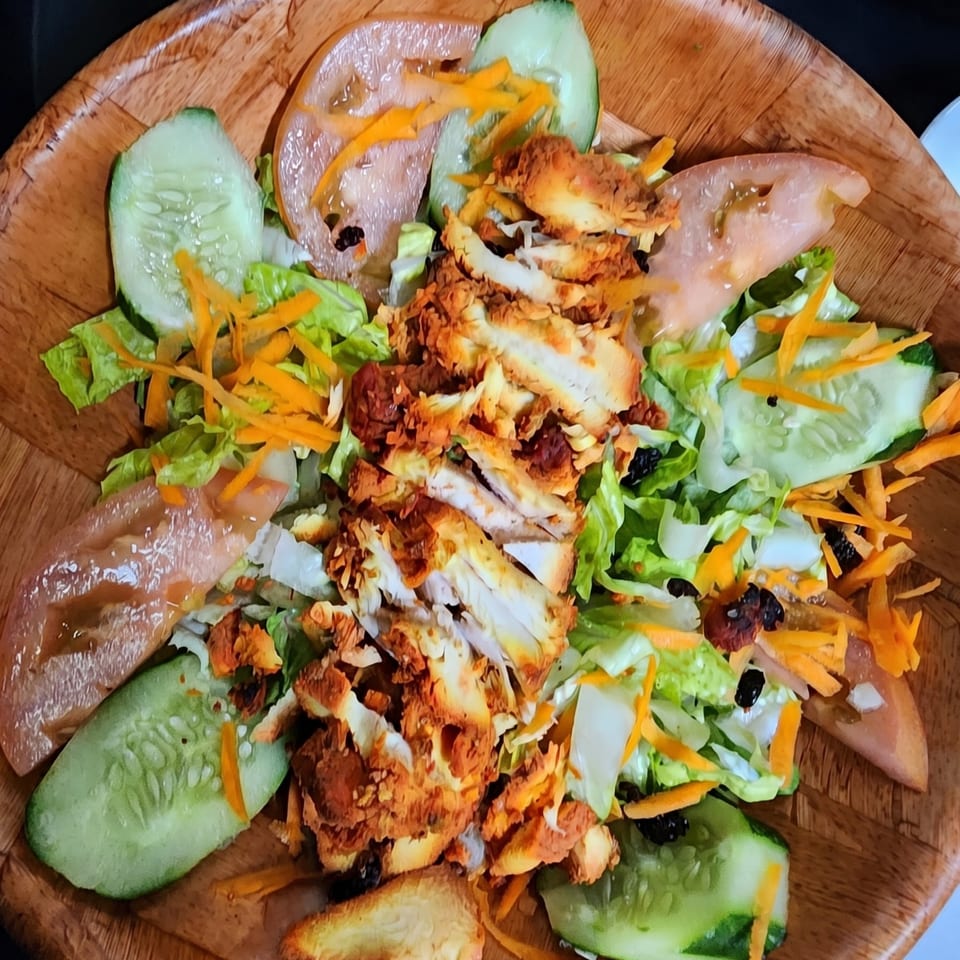 Crispy chicken salad with lettuce, cucumbers, tomatoes, and shredded carrots in a wooden bowl.