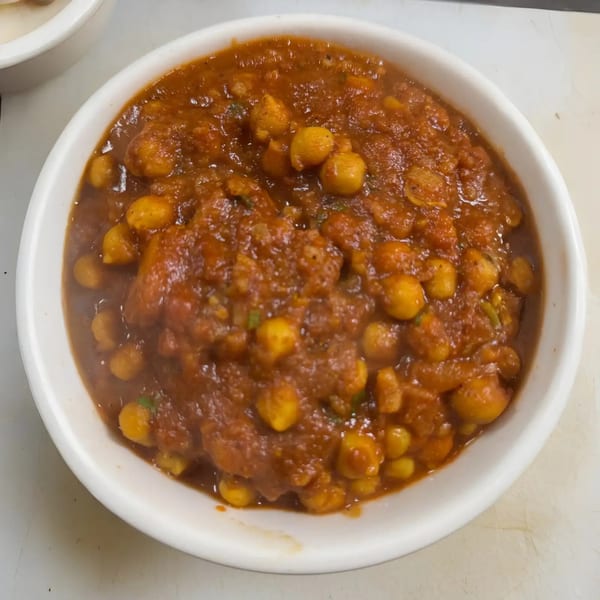 A white bowl filled with chana masala, a chickpea curry in a rich, reddish-brown sauce.