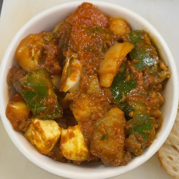 A white bowl filled with paneer, green bell peppers, and onions in a rich red sauce.