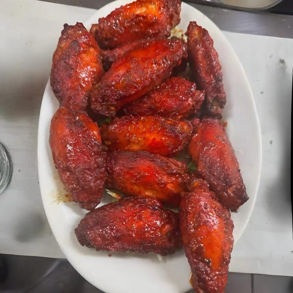 A white plate piled high with glistening, deep red chicken wings, coated in a rich sauce.
