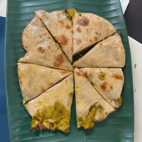 Round flatbread, cut into eight triangular pieces, with a yellow filling, served on a green banana leaf.