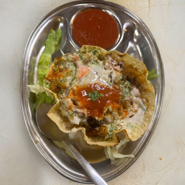A crispy fried tortilla bowl filled with chickpeas, sauces, and fresh cilantro, served with red chili sauce.