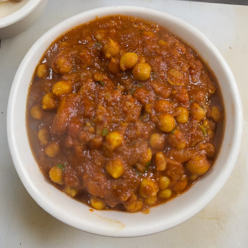 A white bowl filled with chana masala, a chickpea curry in a rich, reddish-brown sauce.