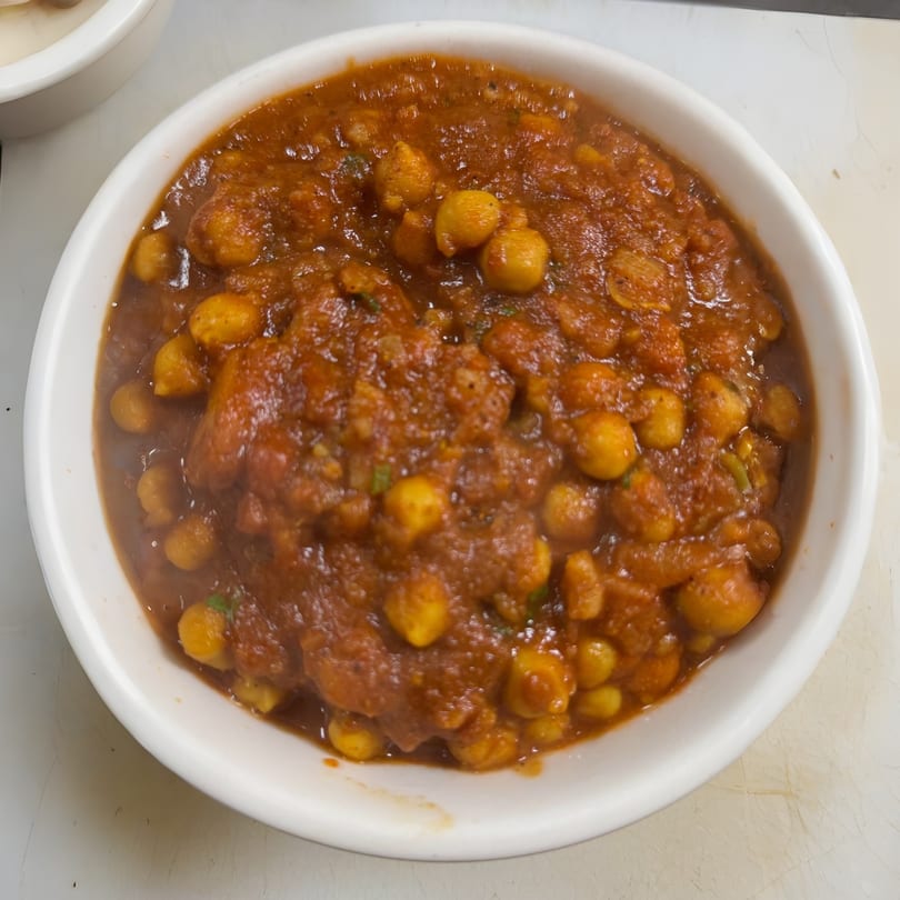 A white bowl filled with chana masala, a chickpea curry in a rich, reddish-brown sauce.